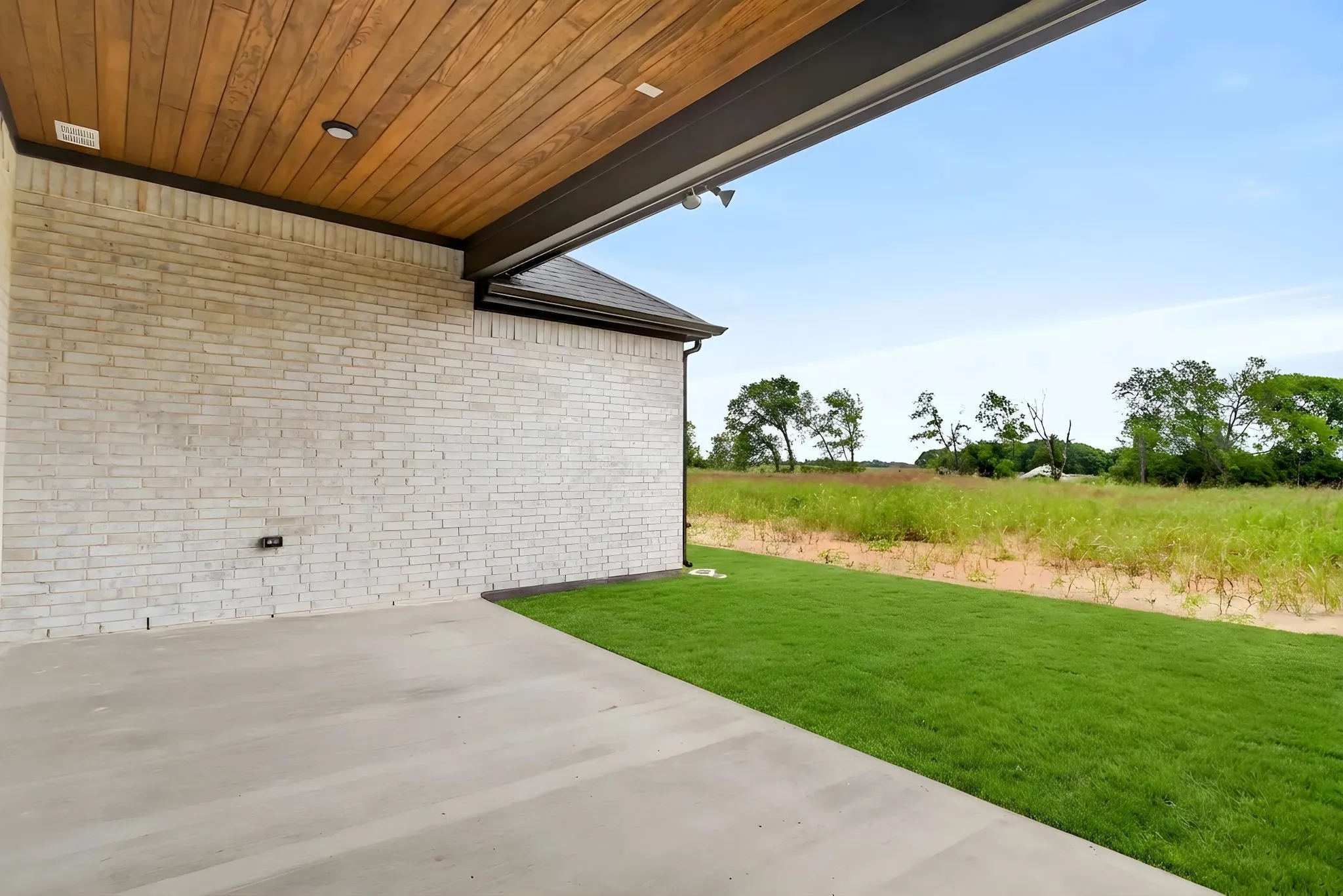 Covered patio with a wood-finish ceiling, integrated recessed lighting, and a light-colored brick exterior