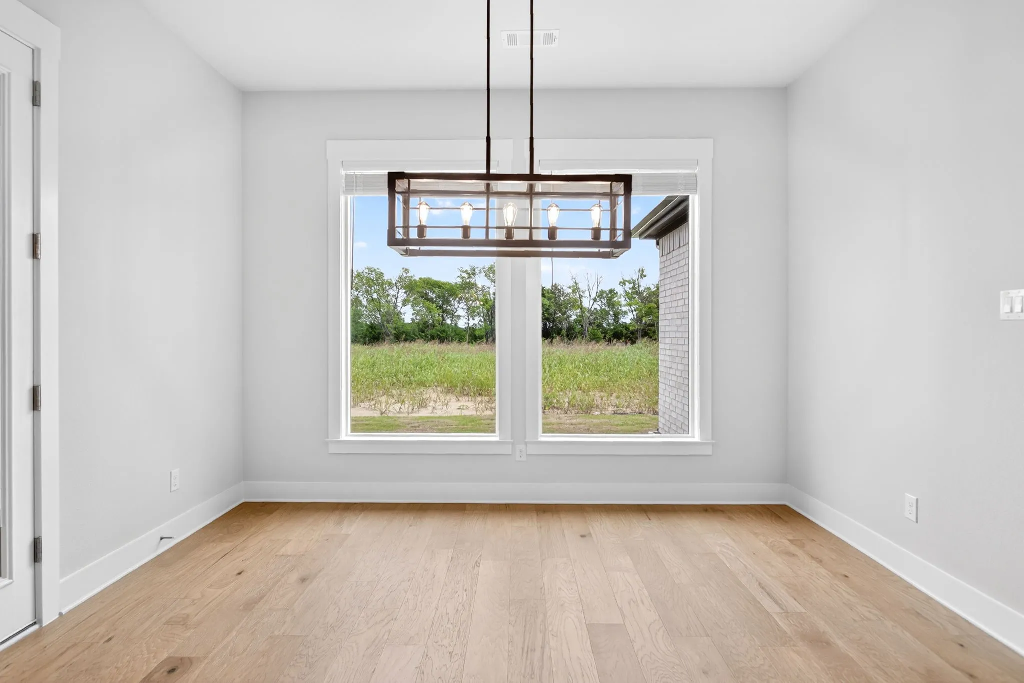 Spacious room featuring wood-finish flooring, white baseboards, and a modern rectangular chandelier