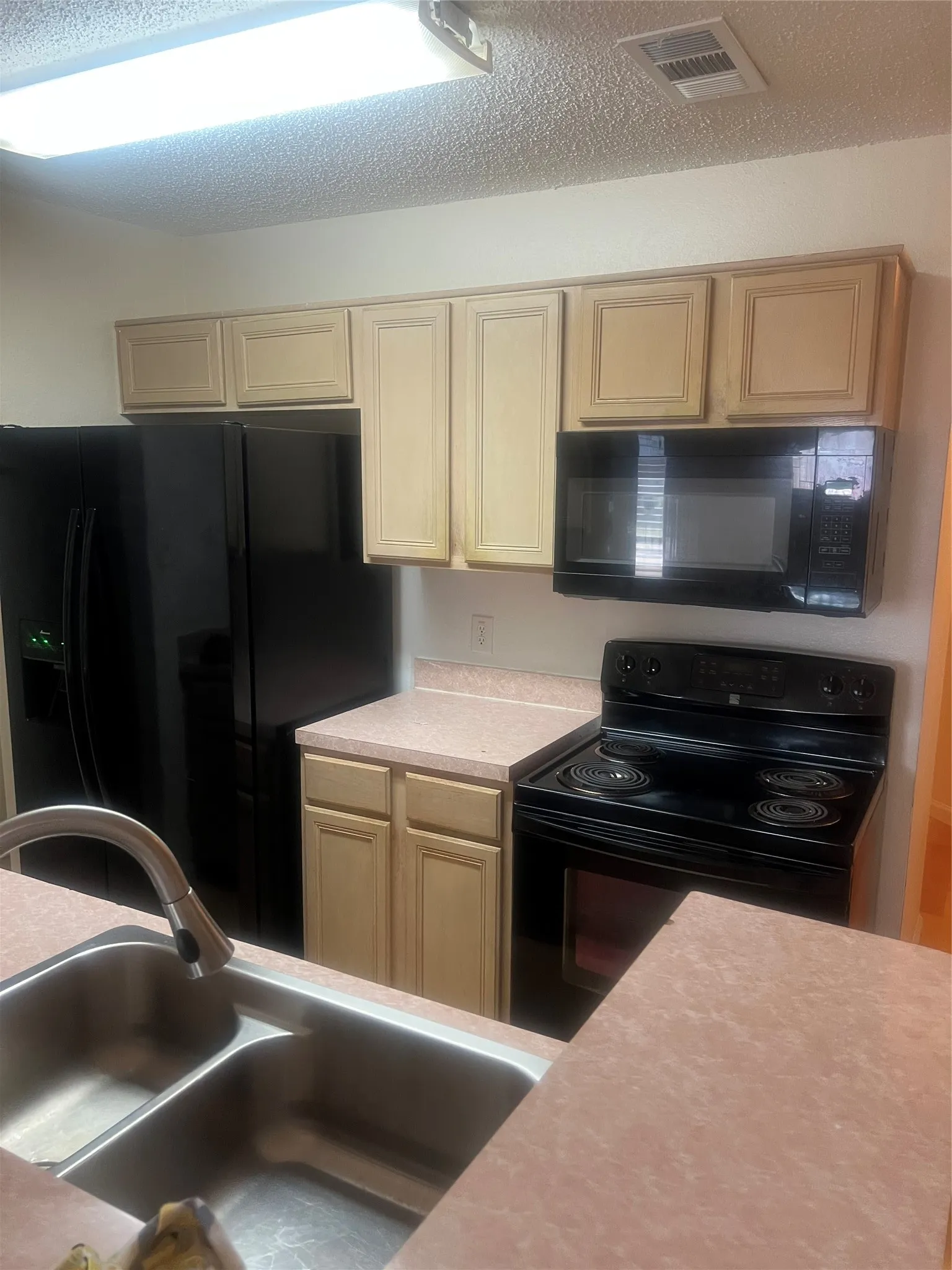 Kitchen featuring a double basin stainless steel sink with a pull-down faucet, black refrigerator, black electric range, and black microwave