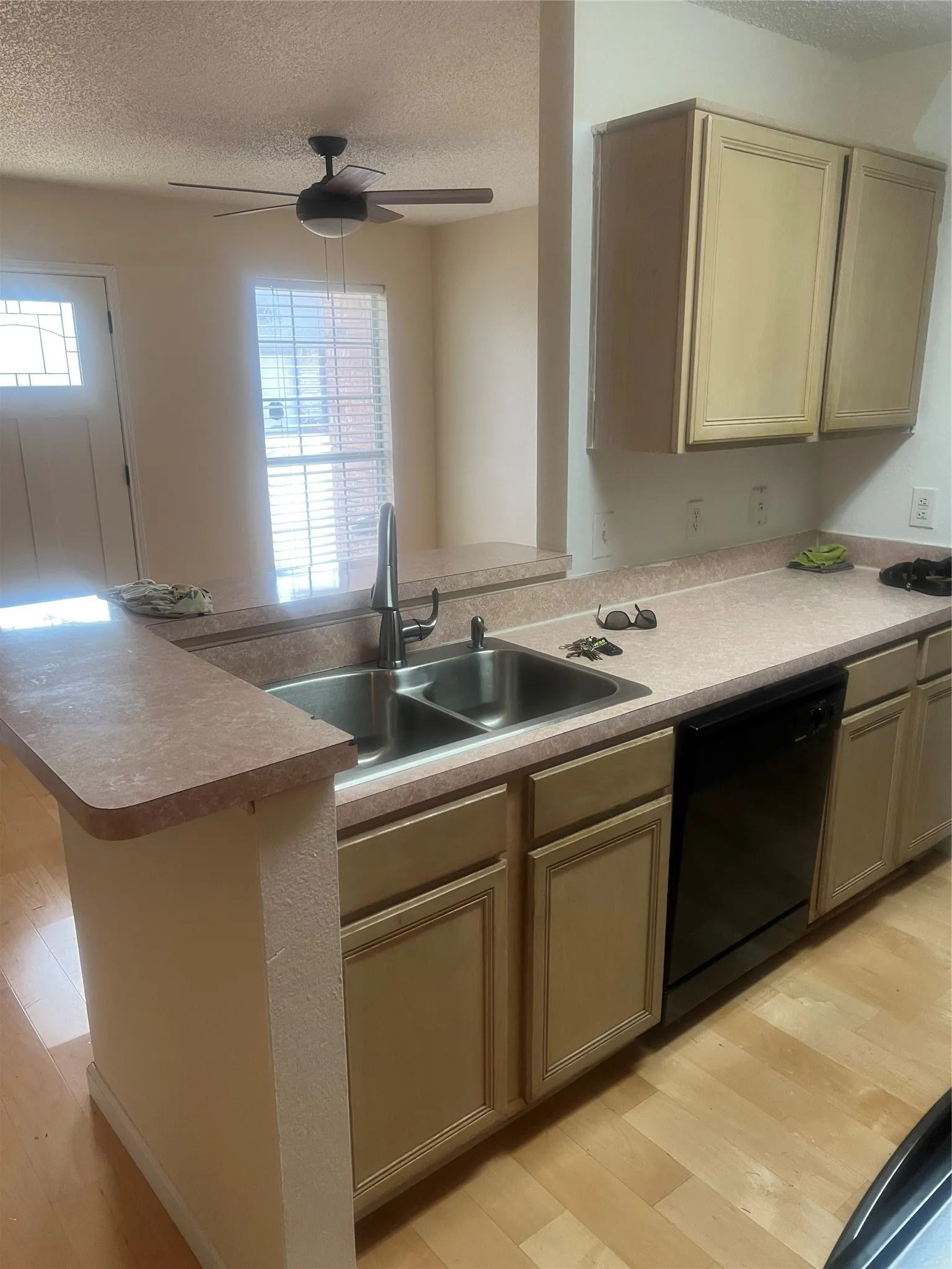 Kitchen area featuring a stainless steel double basin sink with a gooseneck faucet, tan cabinetry, and a black built-in dishwasher