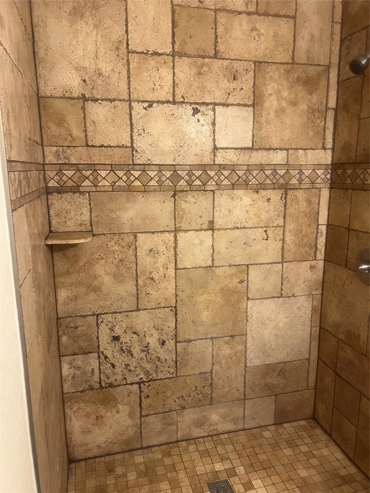 Shower enclosure featuring a mosaic tile border, integrated wall shelf, and coordinating floor tiles