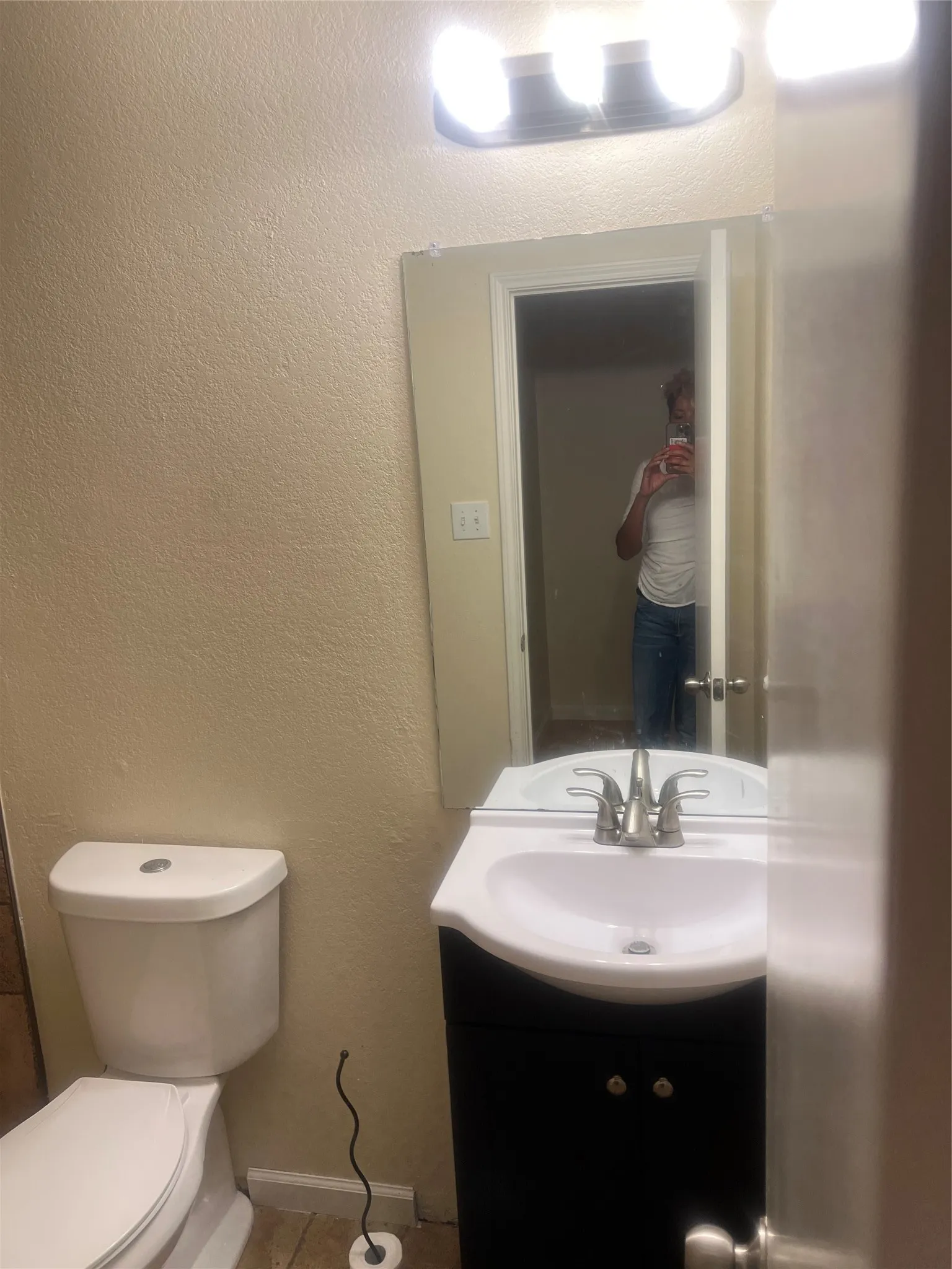 Bathroom featuring a black vanity with an integrated white sink, brushed nickel faucet, wall-mounted mirror, and overhead tri-bulb light fixture
