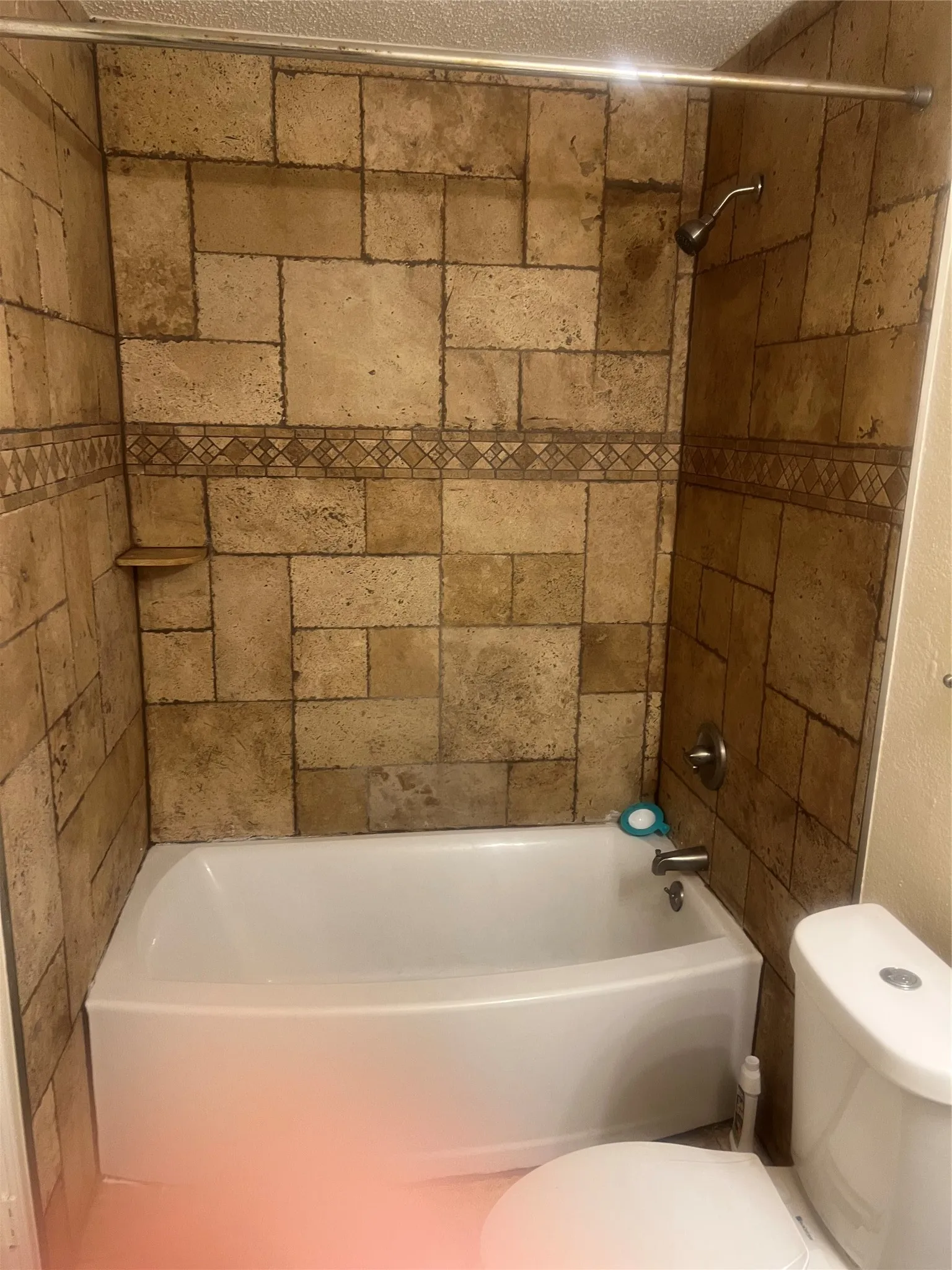 Shower-over-tub combination with textured stone-look tile surround and decorative mosaic accent band
