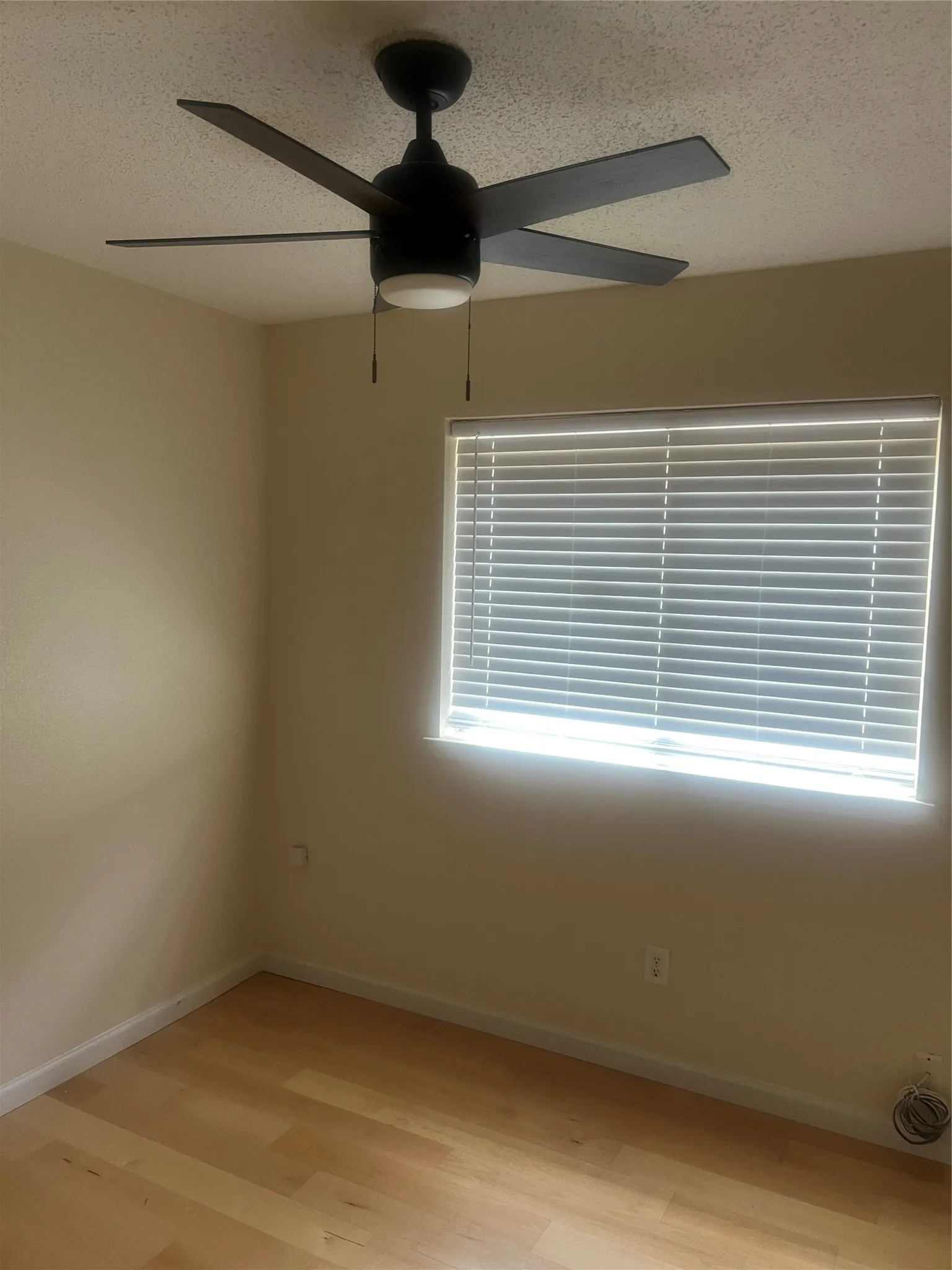 Room featuring light wood-finish flooring, a window with horizontal blinds, and a ceiling fan with integrated lighting