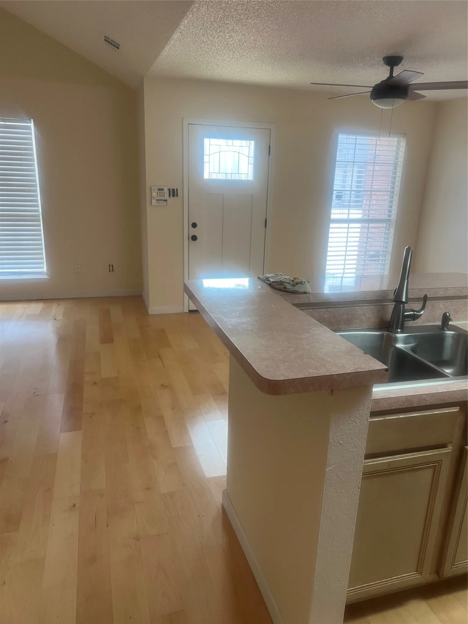 Open-concept space featuring wood-finish flooring, a kitchen peninsula with an integrated sink, a ceiling fan, and a front entry door with decorative glass