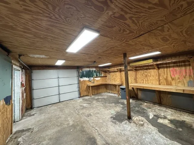 Garage space featuring a paneled overhead door, concrete flooring, and wood-paneled walls and ceiling