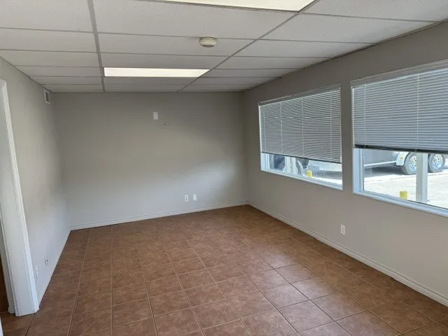 Spacious room featuring tile flooring, neutral wall tones, two large windows with blinds, a drop ceiling with recessed lighting, and white baseboards