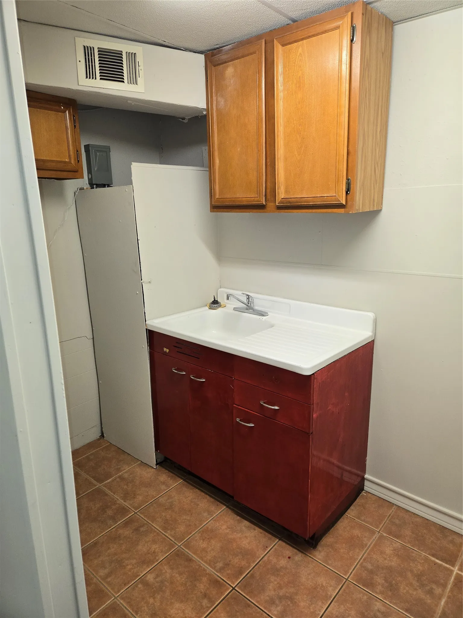 Kitchen area featuring a utility sink with an integrated drainboard, wood-finish base cabinetry, and wood-finish wall-mounted cabinetry
