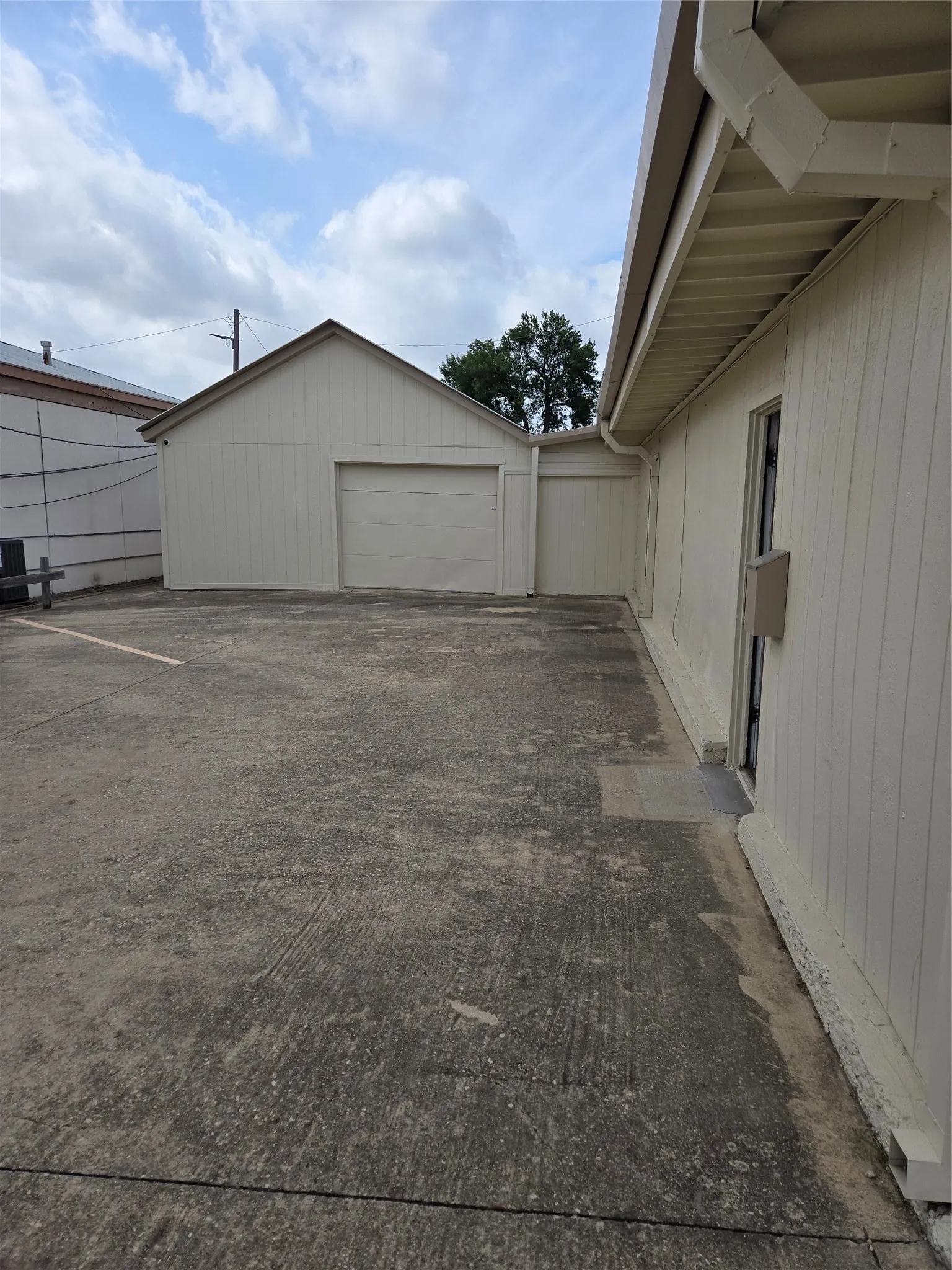 Paved exterior space featuring a detached garage with a roll-up door, vertical siding, and a gabled roofline