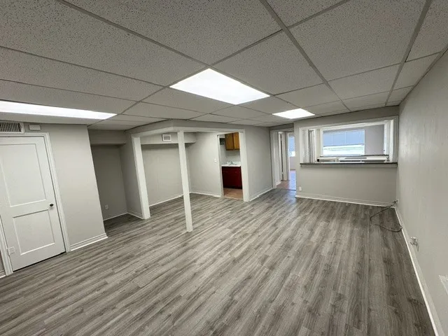Spacious room featuring wood-finish flooring, a drop ceiling with integrated lighting, and light gray wall paint
