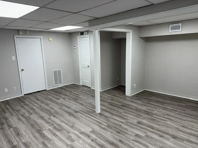 Spacious room featuring wood-finish flooring, light grey painted walls, white trim, and a drop ceiling with recessed lighting