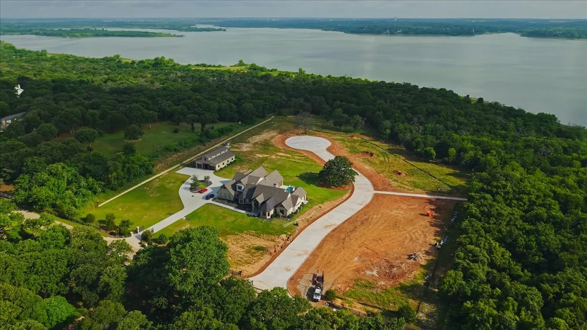 Expansive property featuring a large residence, a separate detached structure, a paved driveway, and substantial cleared land