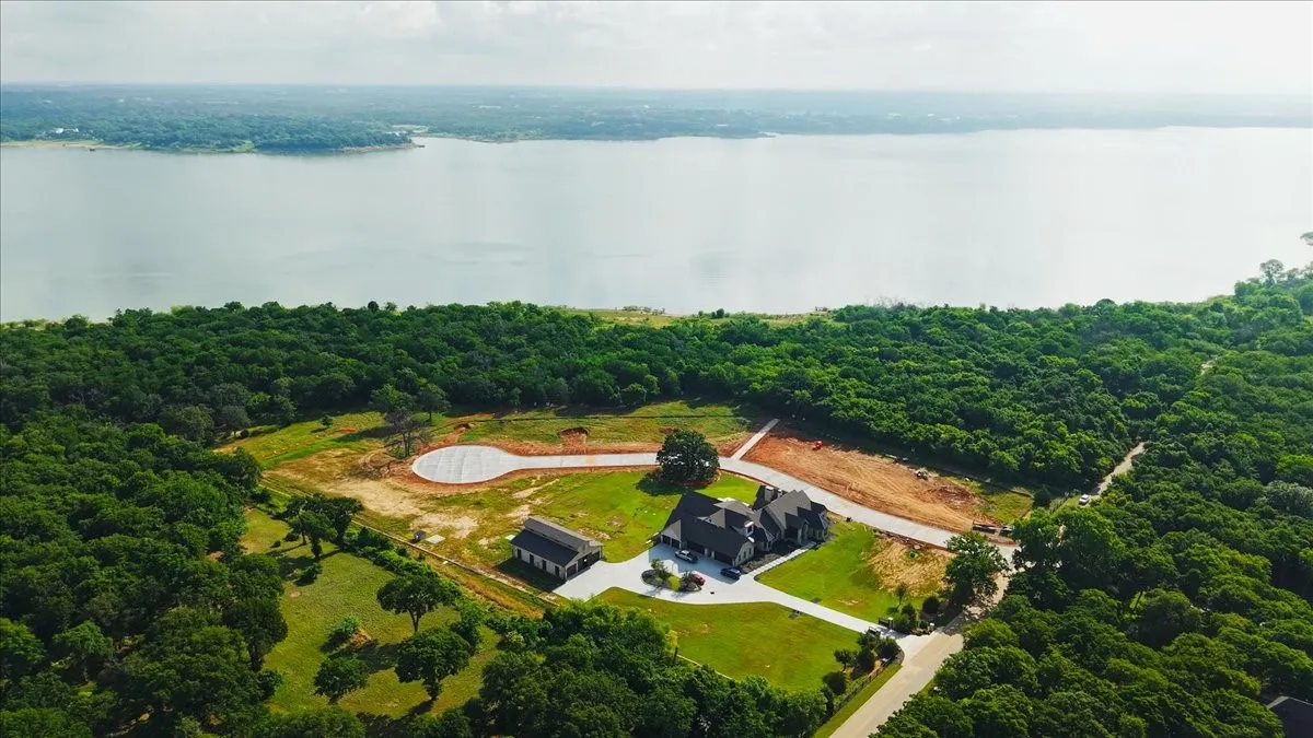 Expansive property featuring a large lakefront, mature tree coverage, a primary residence with an attached garage, a separate outbuilding, and a paved driveway