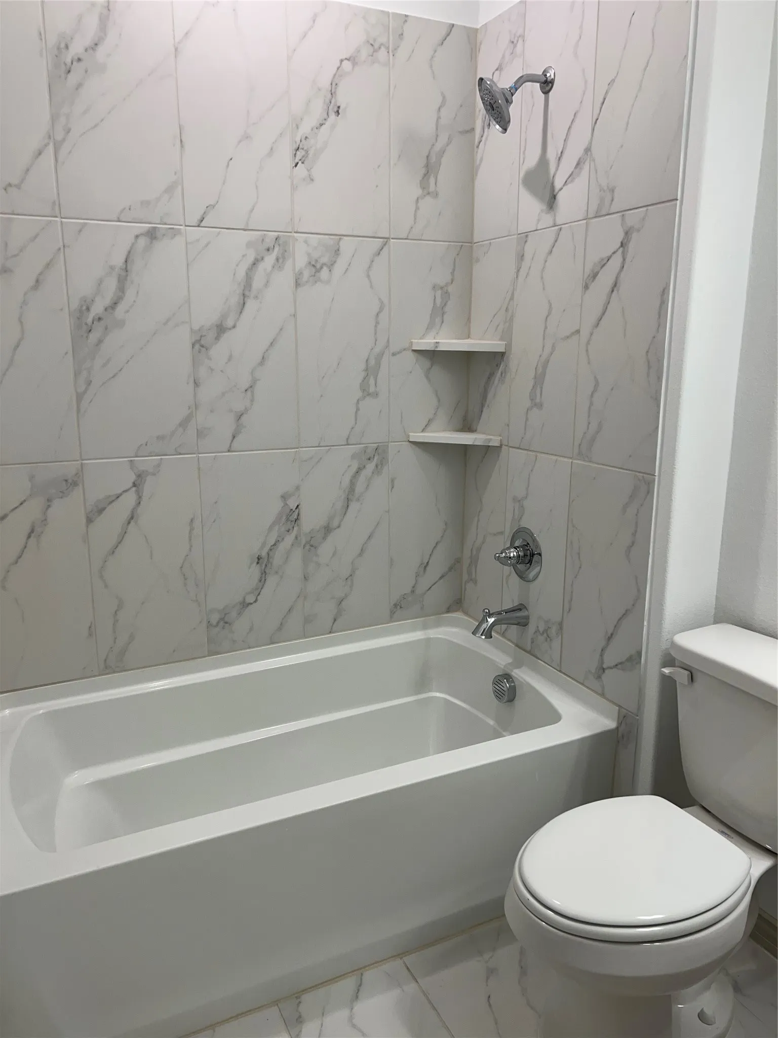 Bathtub and shower combination featuring white marble-look tile surround and chrome fixtures