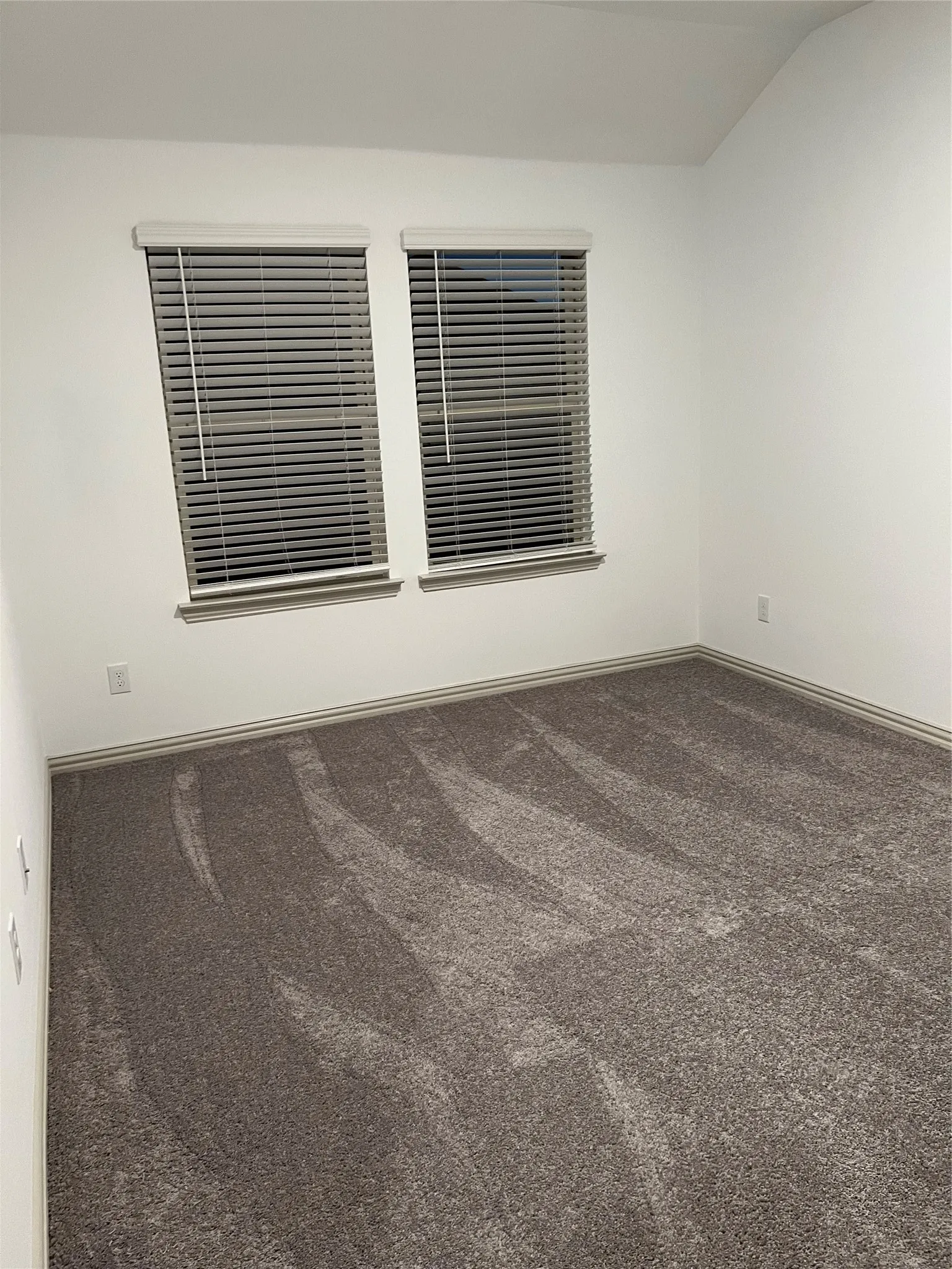 Carpeted interior space featuring white walls and a vaulted ceiling