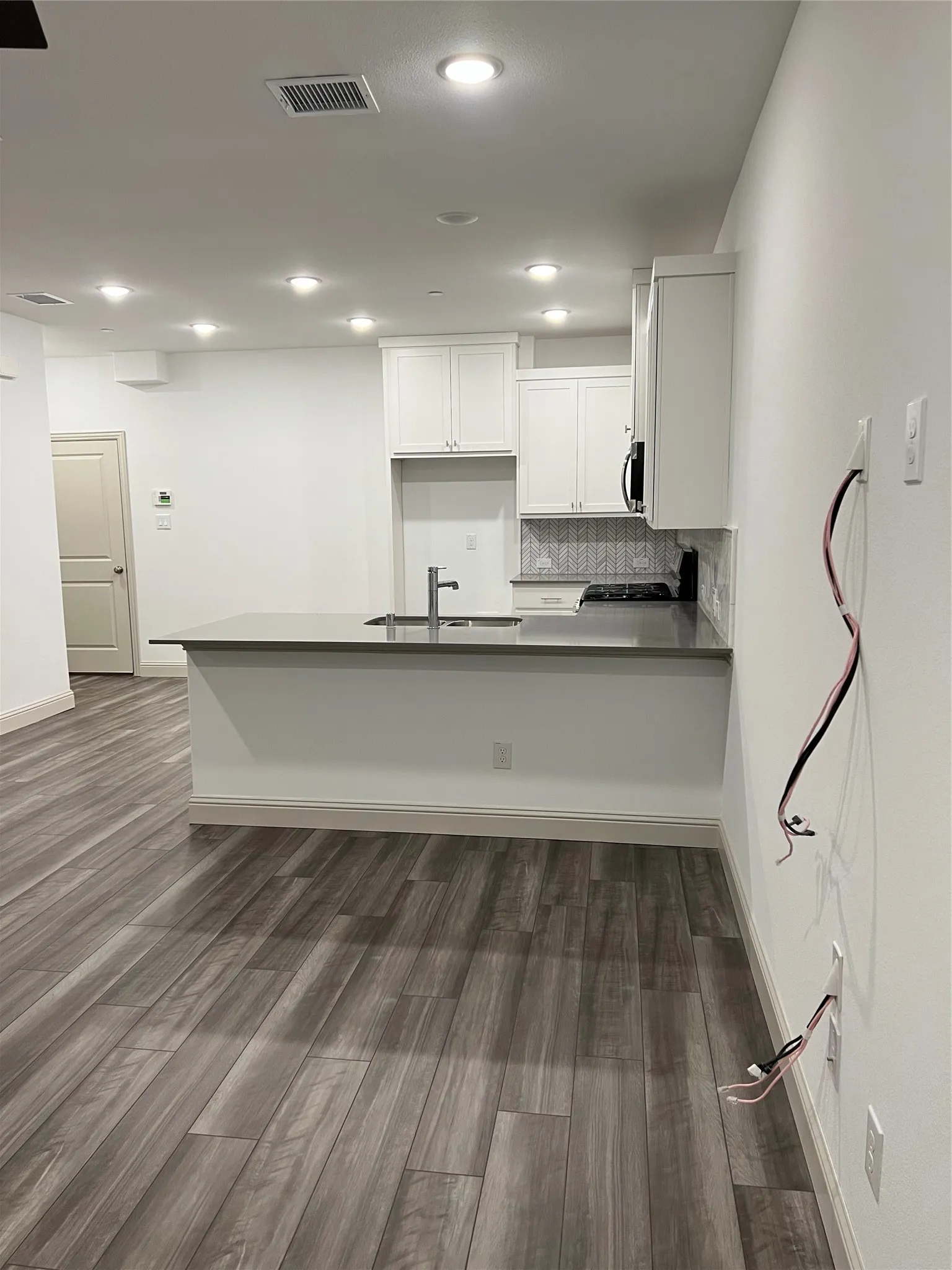 Modern kitchen featuring white cabinetry, a gray solid surface countertop island with integrated sink, and a contrasting tile backsplash