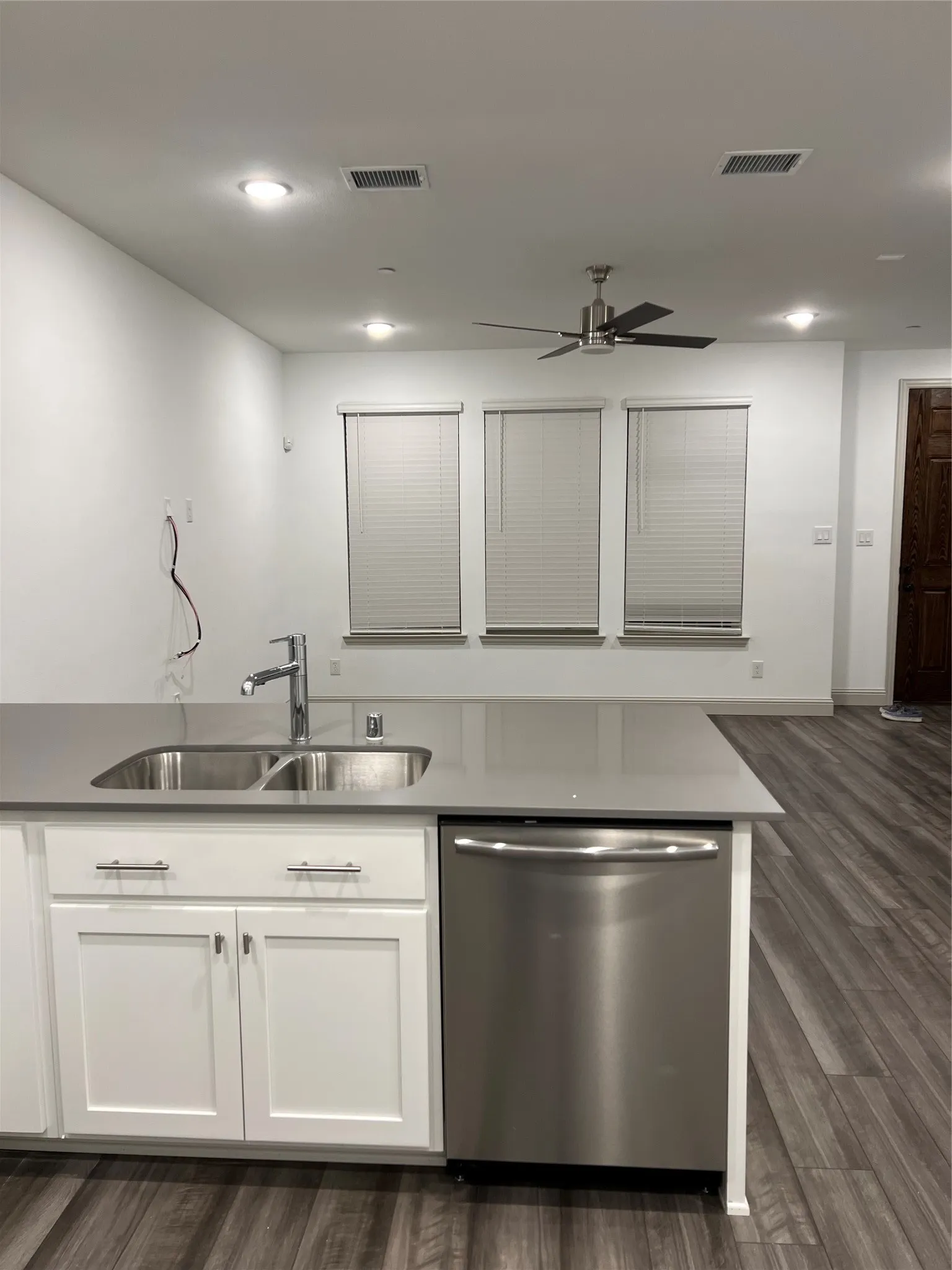 Kitchen island featuring a double basin stainless steel sink, a stainless steel dishwasher, white shaker cabinetry with brushed nickel hardware, and a solid surface countertop