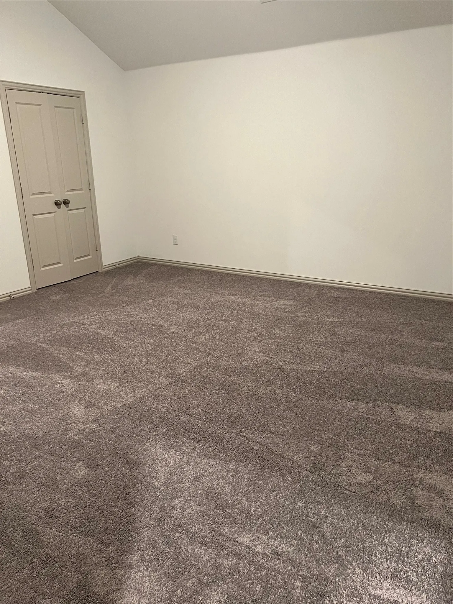 Spacious room featuring vaulted ceilings, light-toned walls, and a neutral carpet