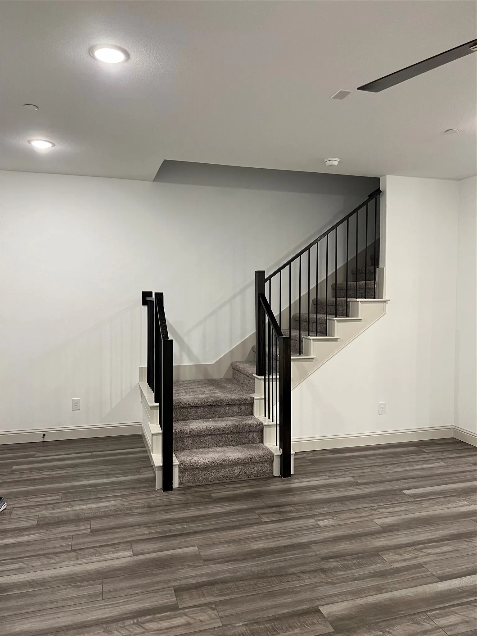 Staircase featuring dark carpet treads, white risers, and black metal balusters