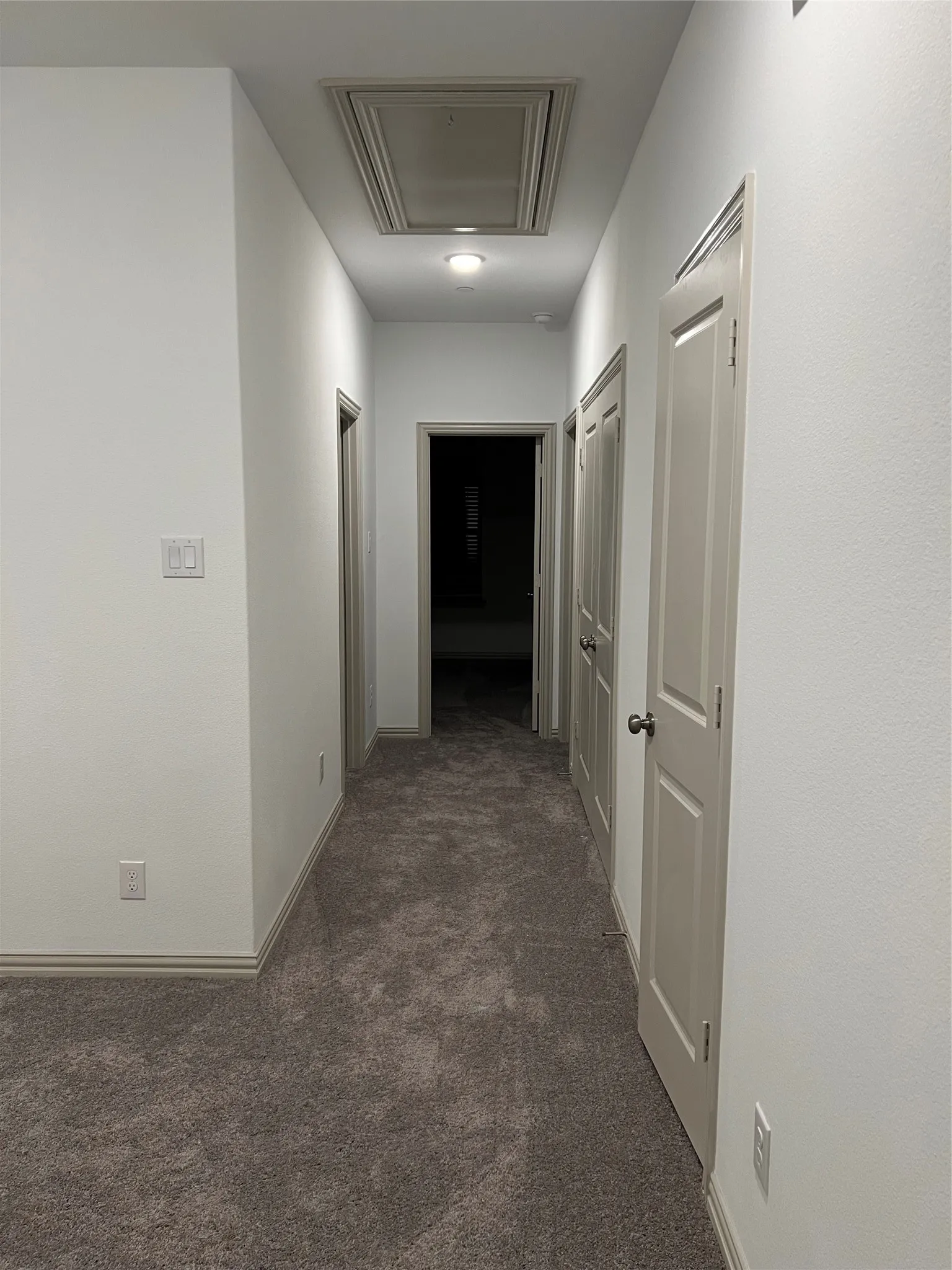 Hallway with neutral tone carpeting and crisp white walls