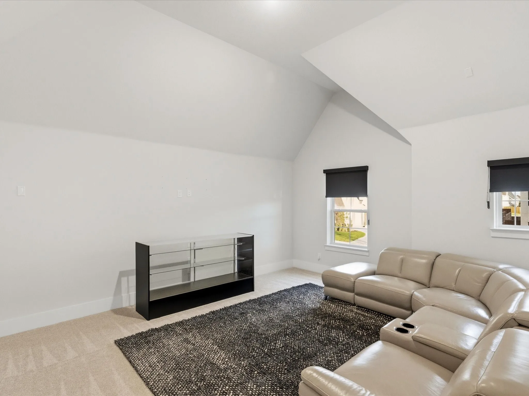 Spacious bonus room featuring vaulted ceilings, two windows with roller shades, and light neutral carpeting