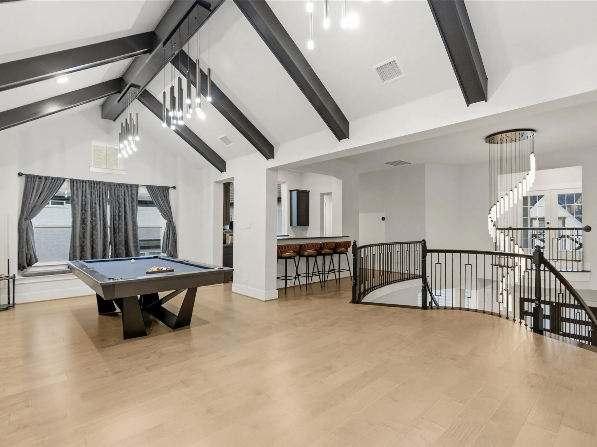 Open entertainment area with vaulted ceilings, exposed dark beams, and light wood-finish flooring
