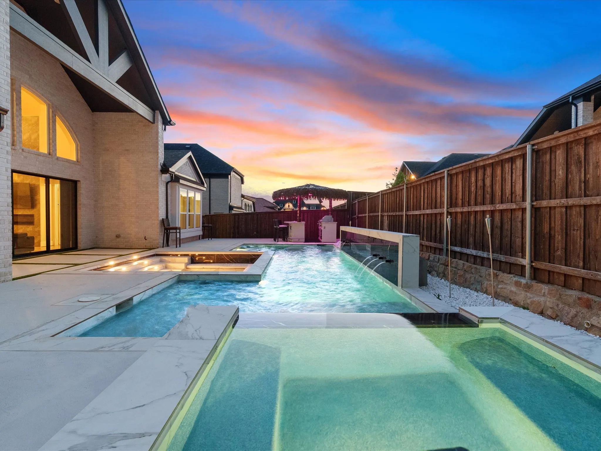 Expansive pool area featuring multiple water features, integrated spa, and a light-colored paver patio