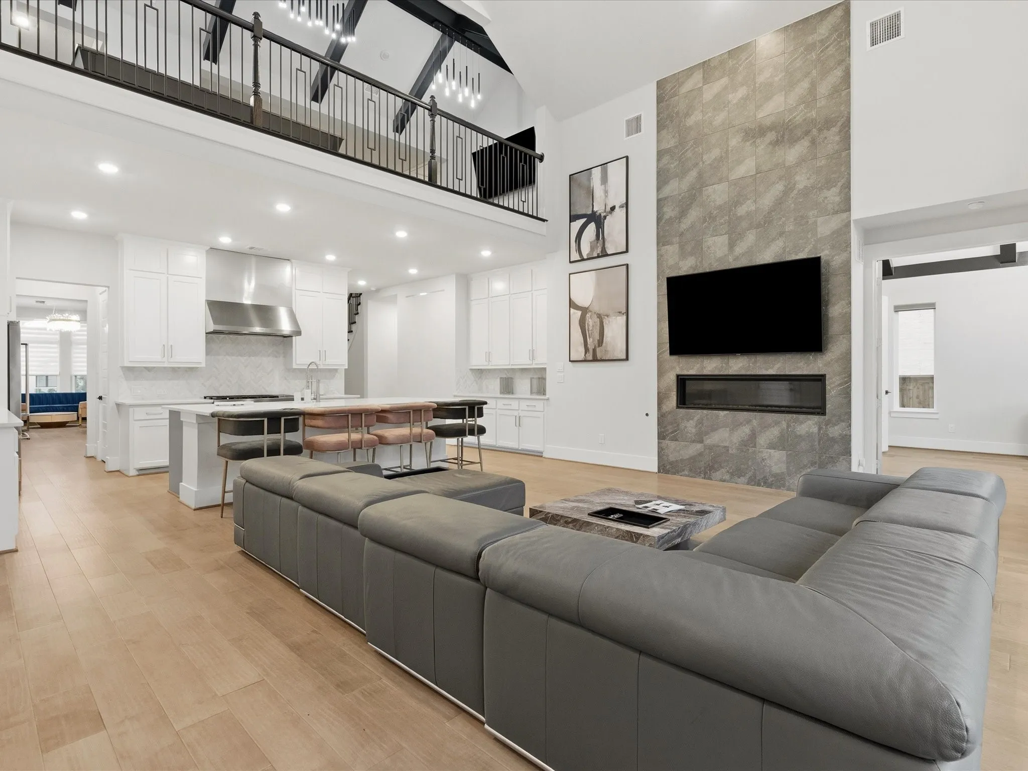 Open-concept living space featuring wood-finish flooring, a two-story tiled fireplace wall with an integrated linear firebox, and a gourmet kitchen with a central island