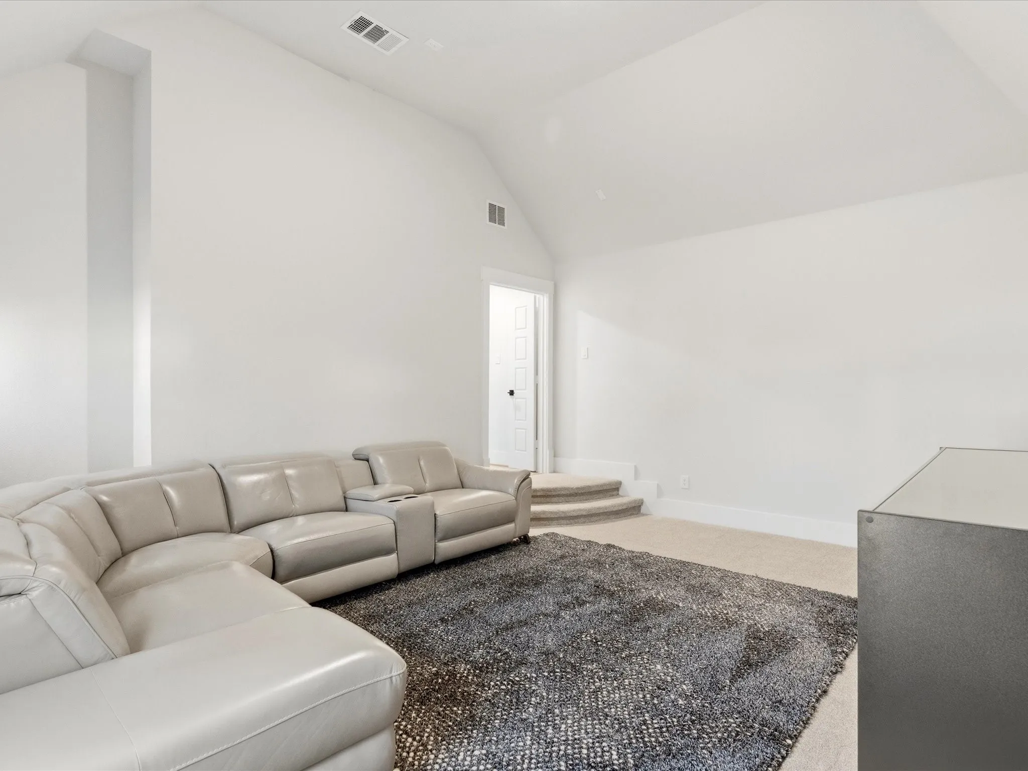 Spacious room featuring a vaulted ceiling, neutral wall tones, and plush carpet flooring