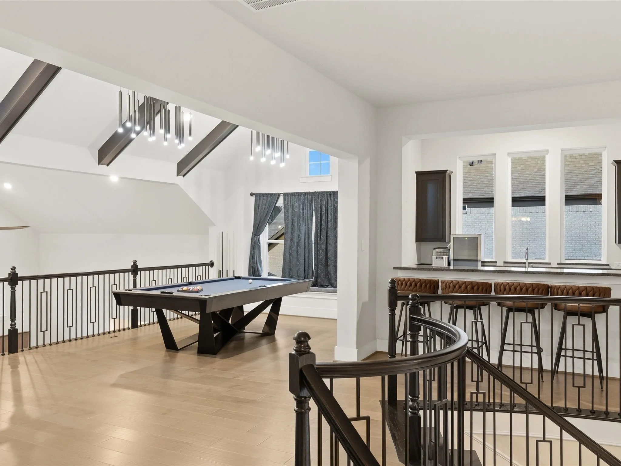 Loft space featuring light wood-finish flooring, a contemporary billiards table, and a wet bar with dark cabinetry and countertop