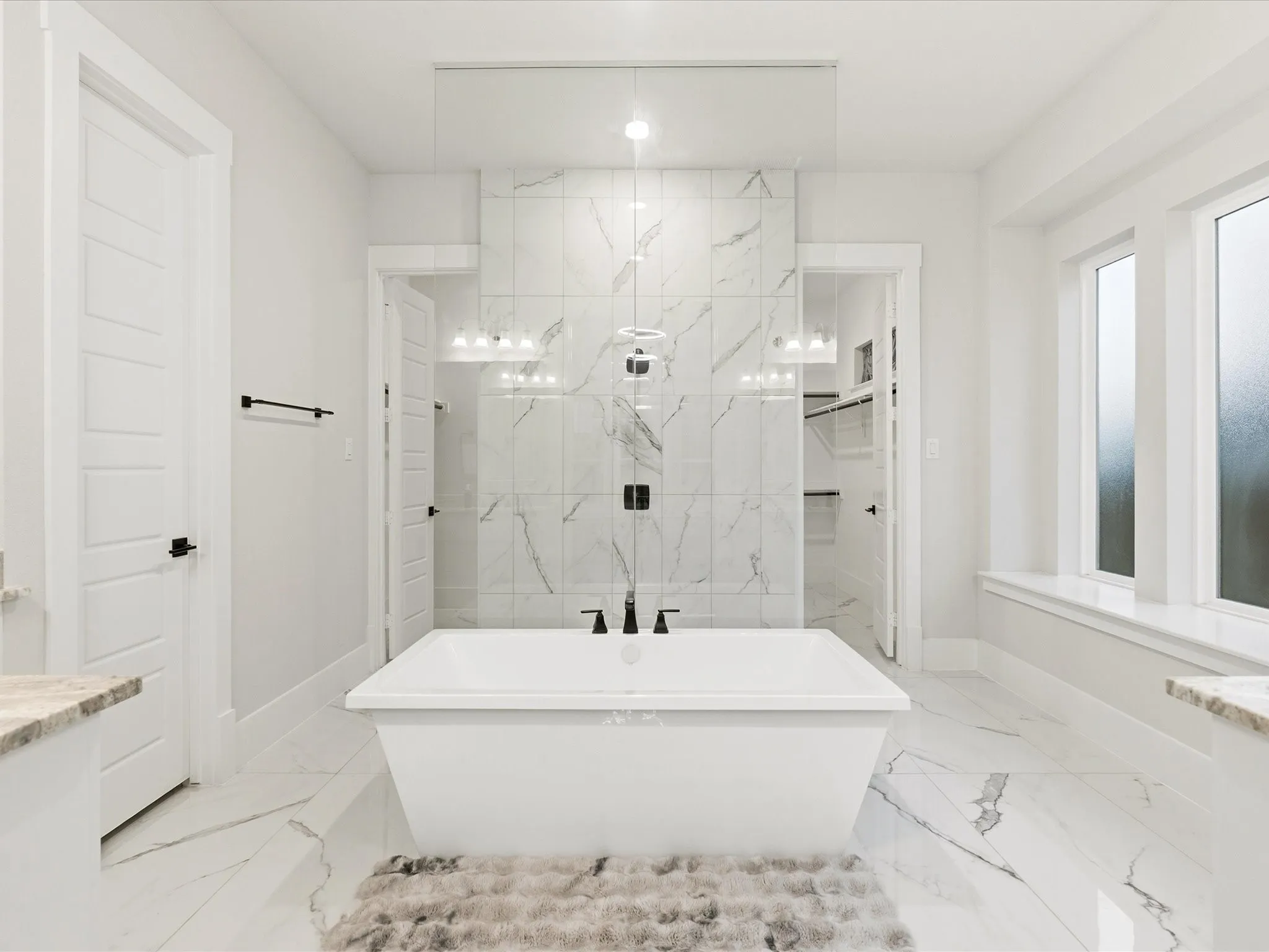 Freestanding soaking tub with matte black fixtures centered on a full-height tile accent wall