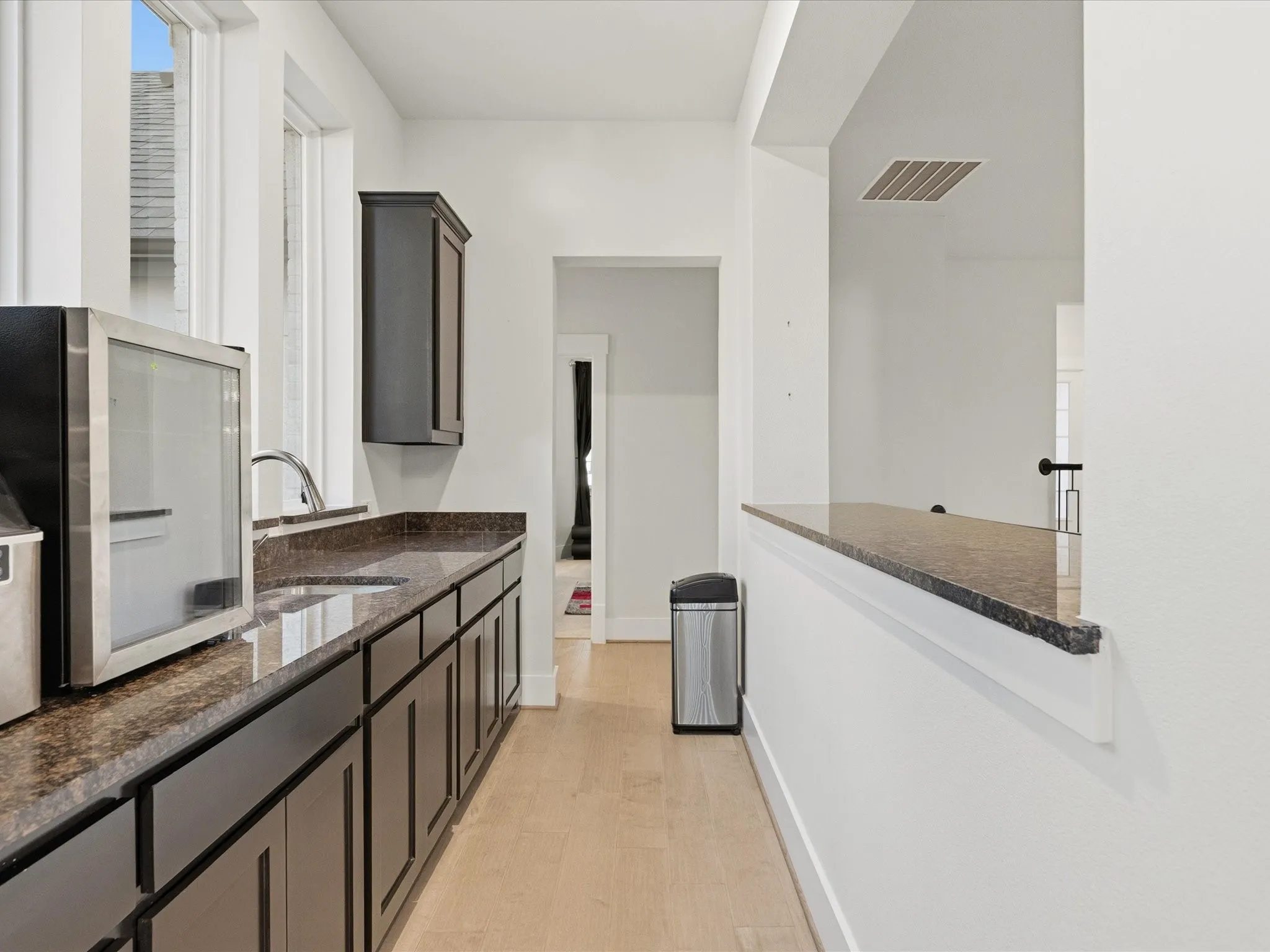 Wet bar featuring dark wood-finish cabinetry, a single basin sink with a gooseneck faucet, and light wood-finish flooring