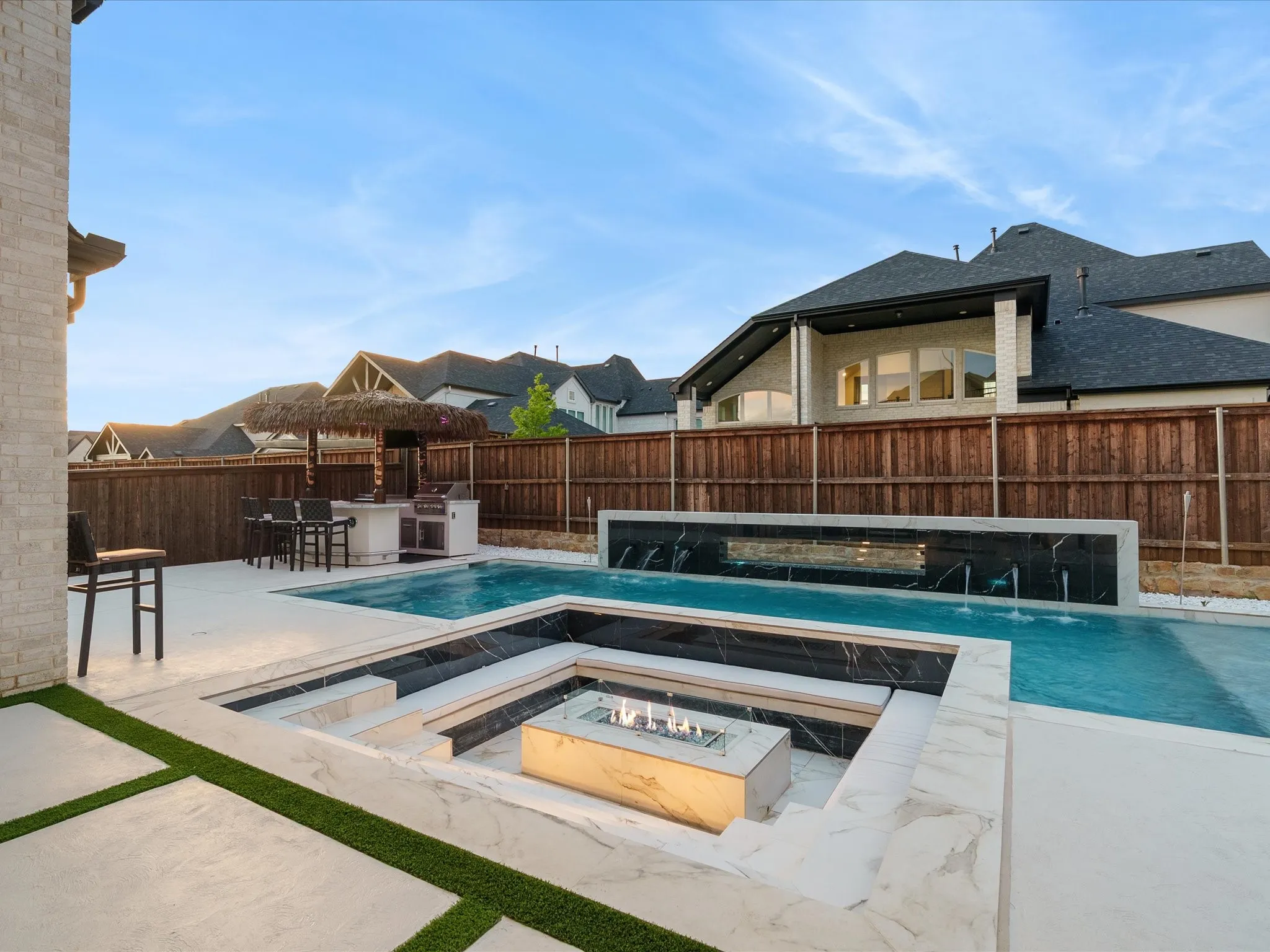 Outdoor living space featuring a multi-level pool with a fire pit, water features, and an outdoor kitchen with a thatched-roof bar