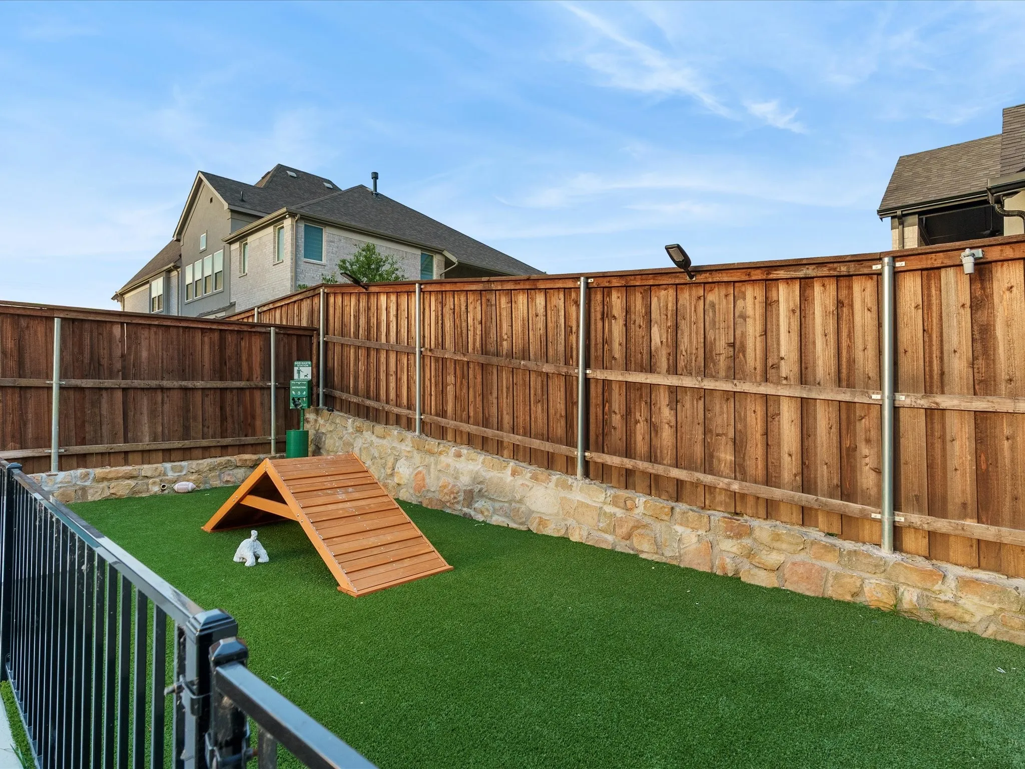 Dedicated pet area featuring artificial turf, a wood ramp, and a black wrought iron fence