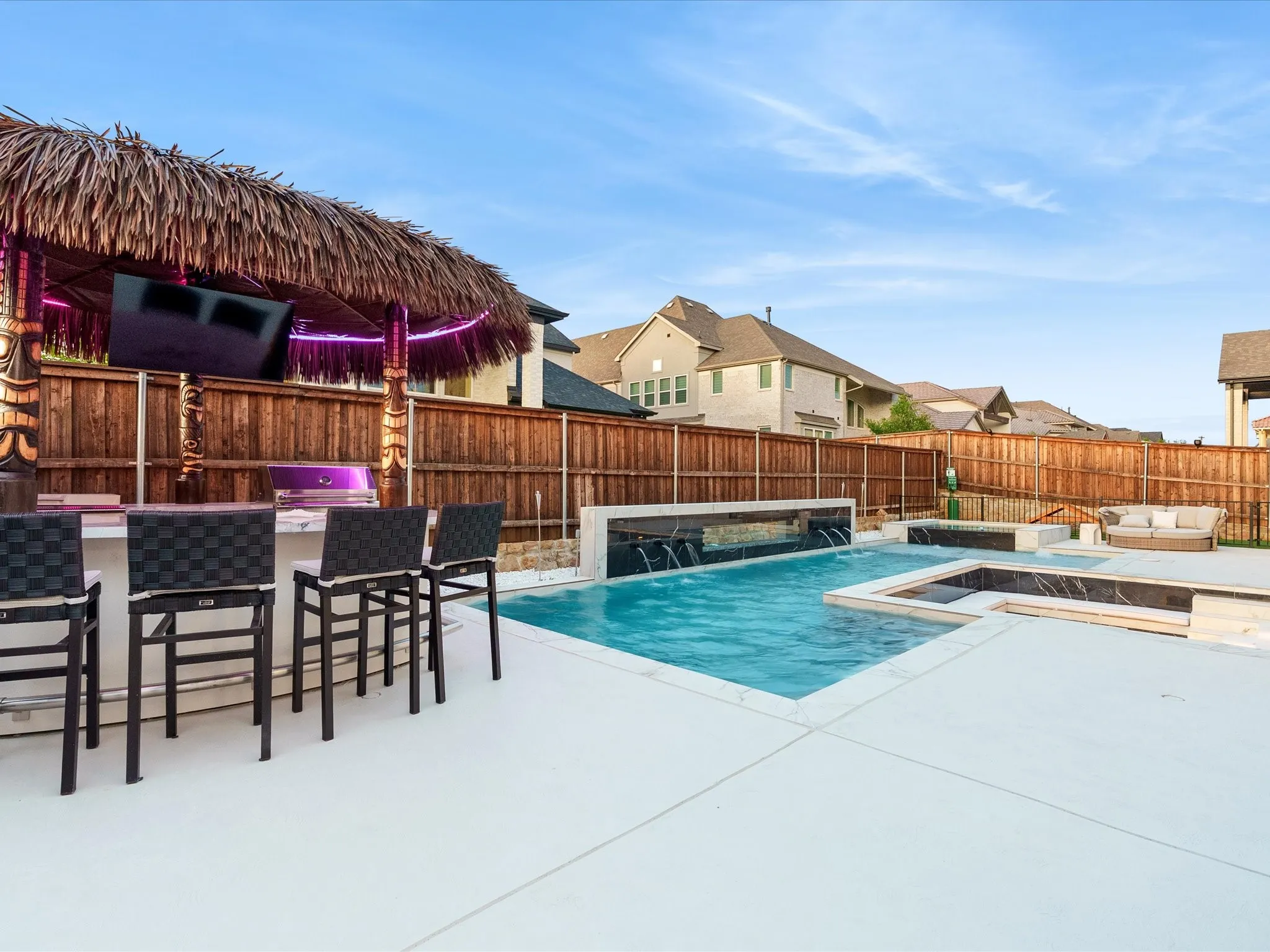 Backyard entertainment area featuring a thatched-roof bar with built-in appliances, a flat-screen television, and integrated lighting