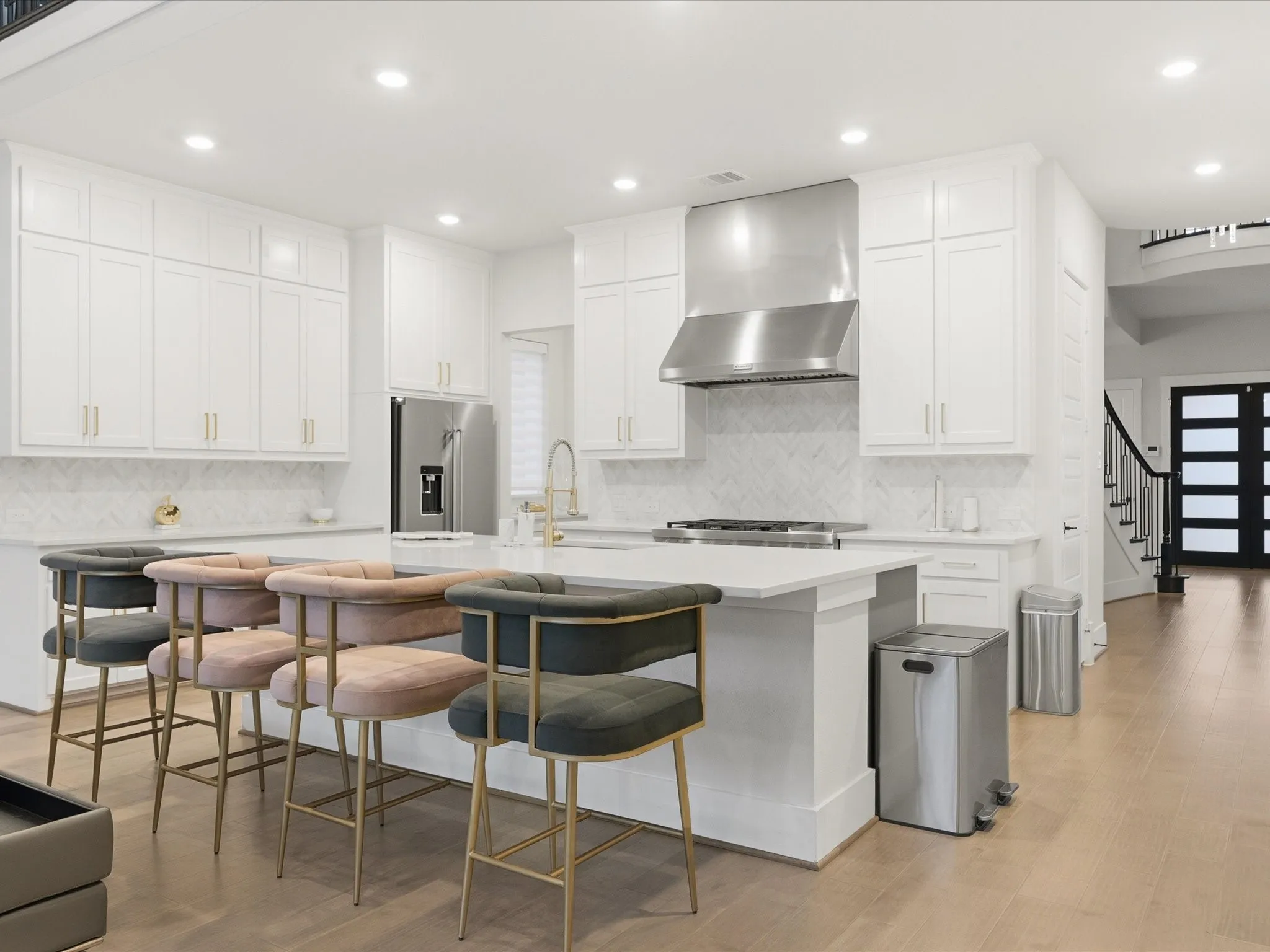 Modern kitchen featuring an expansive center island, white cabinetry, a herringbone tile backsplash, stainless steel appliances, and light wood-finish flooring