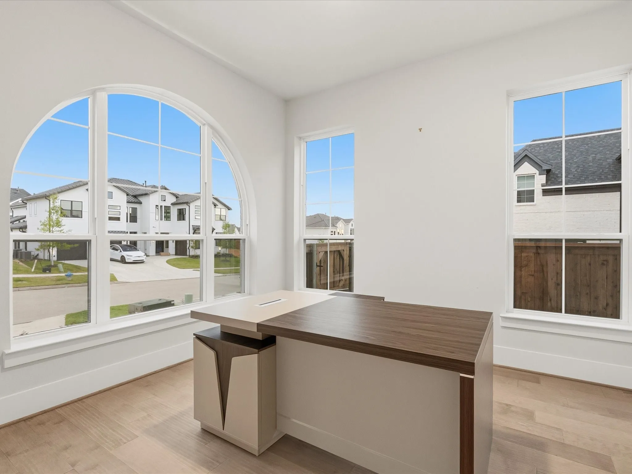 Bright room featuring a large arched window with multiple panes, two additional rectangular windows, wood-finish flooring, and white baseboards