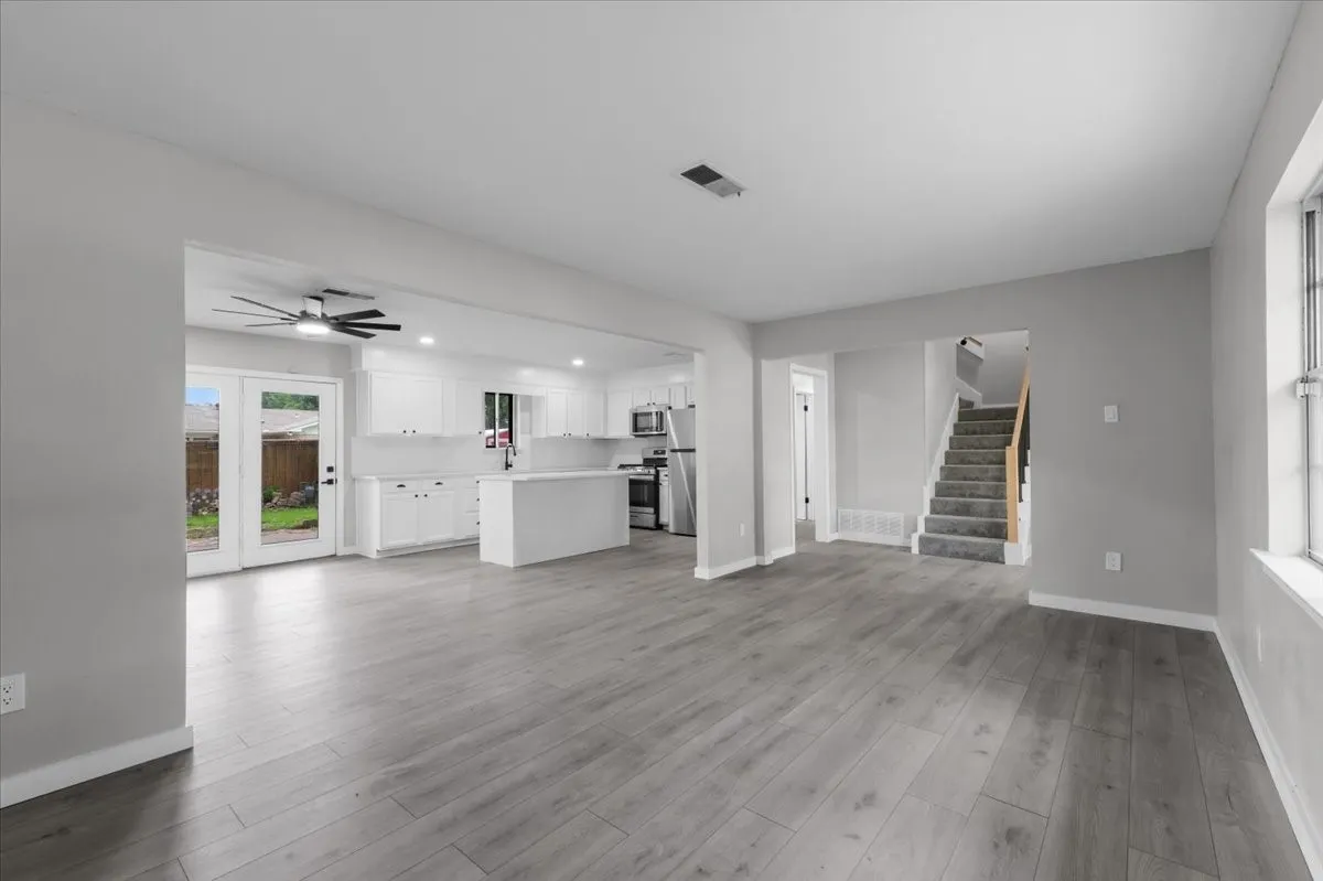 Expansive main living area featuring wood-finish flooring, a white kitchen with an island, and white cabinetry