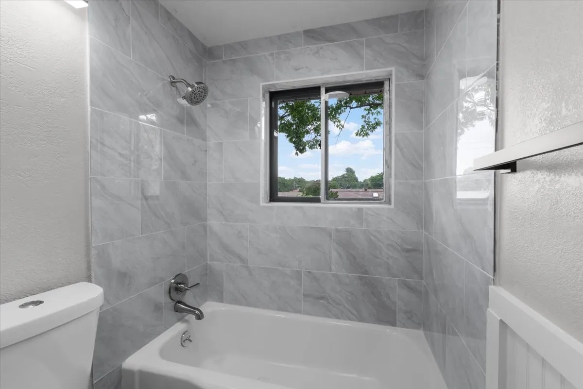 Bathroom featuring a white bathtub with a chrome showerhead and faucet, surrounded by gray large-format wall tiling