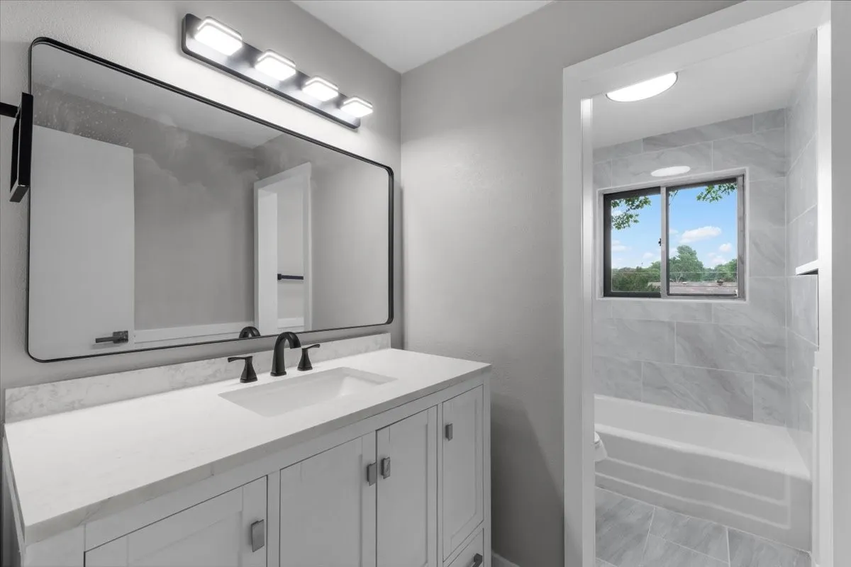 Bathroom featuring a white vanity with integrated sink, rectangular black-framed mirror, and a black multi-bulb light fixture