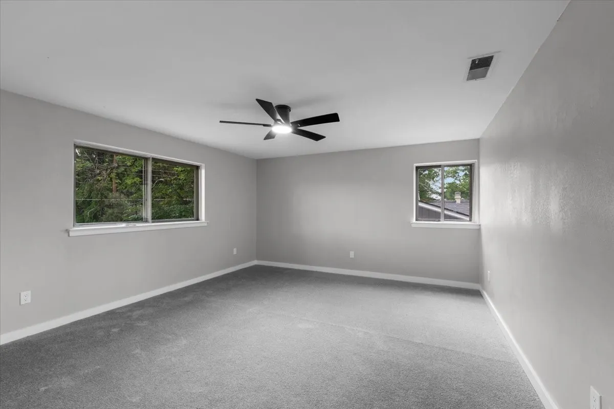Spacious room featuring neutral grey wall paint, plush grey carpeting, and a contemporary ceiling fan with integrated lighting