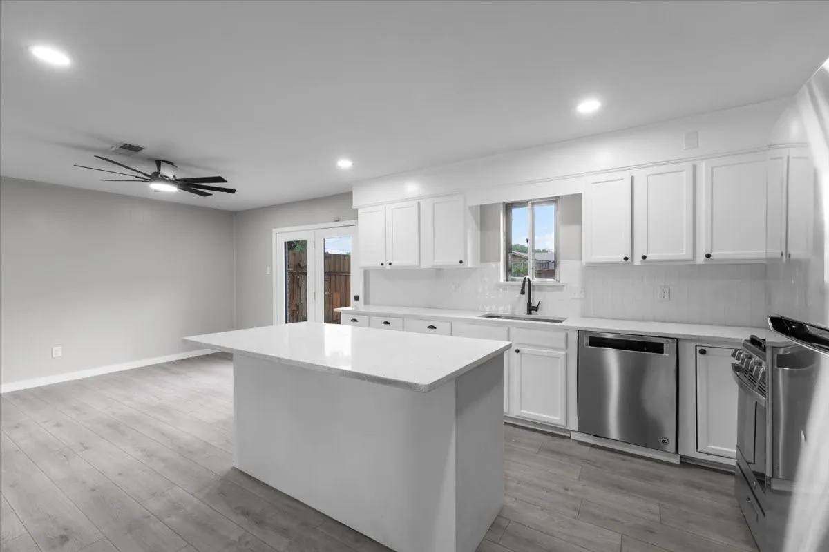 Modern kitchen featuring a central island with a solid surface countertop, white cabinetry with black hardware, stainless steel appliances, and a subway tile backsplash