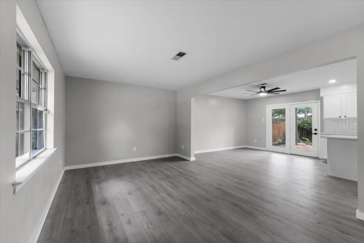 Spacious living area featuring wood-finish flooring, ample natural light from a multi-pane window, and a contemporary ceiling fan