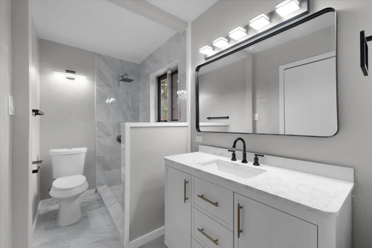 Contemporary bathroom featuring a light gray vanity with a white countertop and gold-toned hardware
