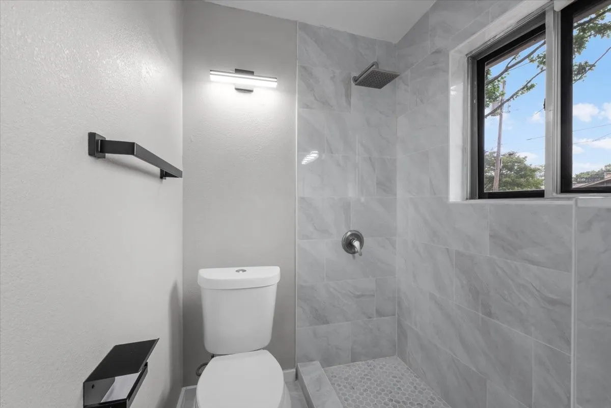 Shower with floor-to-ceiling marble-look tile, rain shower head, and mosaic tile flooring