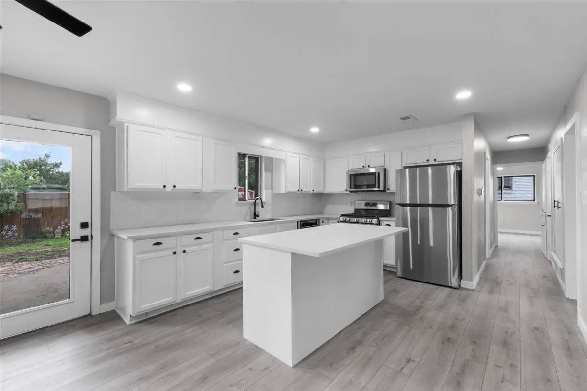 Modern kitchen featuring white cabinetry with black hardware, stainless steel appliances, a center island, light-toned wood-finish flooring, and recessed lighting