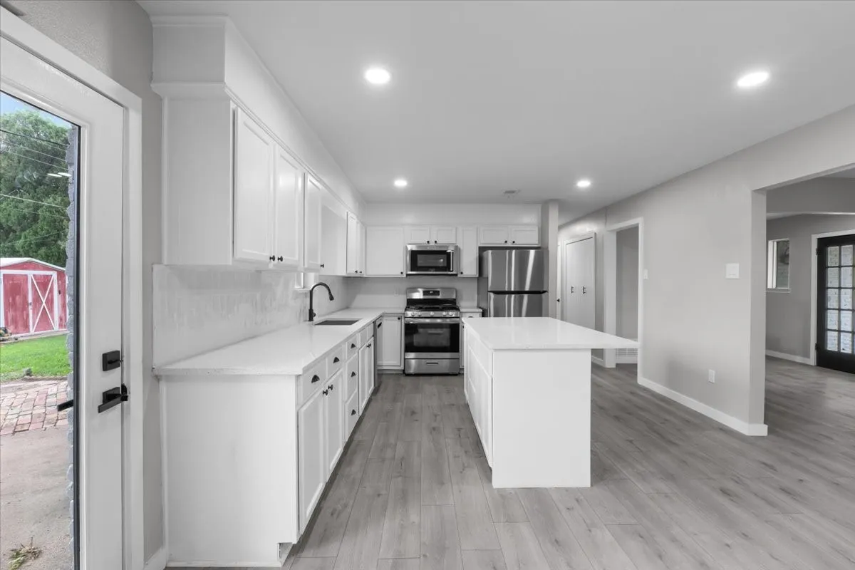 Modern kitchen featuring white shaker cabinetry, stainless steel appliances, light-toned wood-finish flooring, a central island with an extended countertop, and recessed ceiling lighting