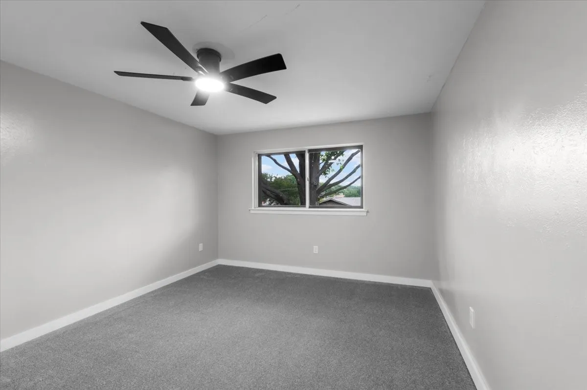 Room featuring light gray walls, gray carpet flooring, a white window trim, and a black ceiling fan with an integrated light