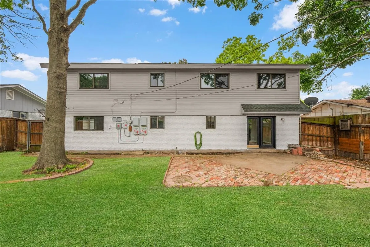 Expansive backyard featuring a manicured lawn, established shade trees, and a brick paver patio