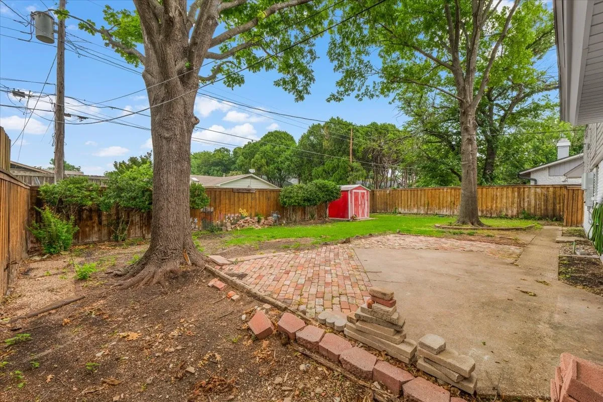 Spacious backyard with mature trees, brick patio, and wooden privacy fencing